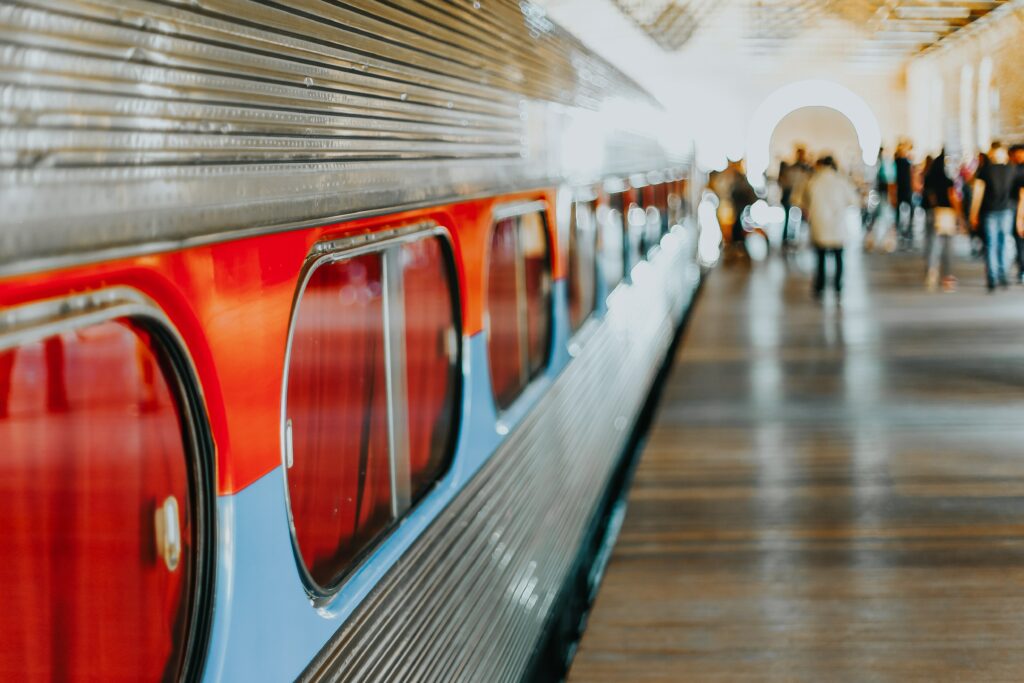 Les transports en vacances.
Photo d'un train à quai dans une gare avec quelques voyageurs floutés dans le fond.
